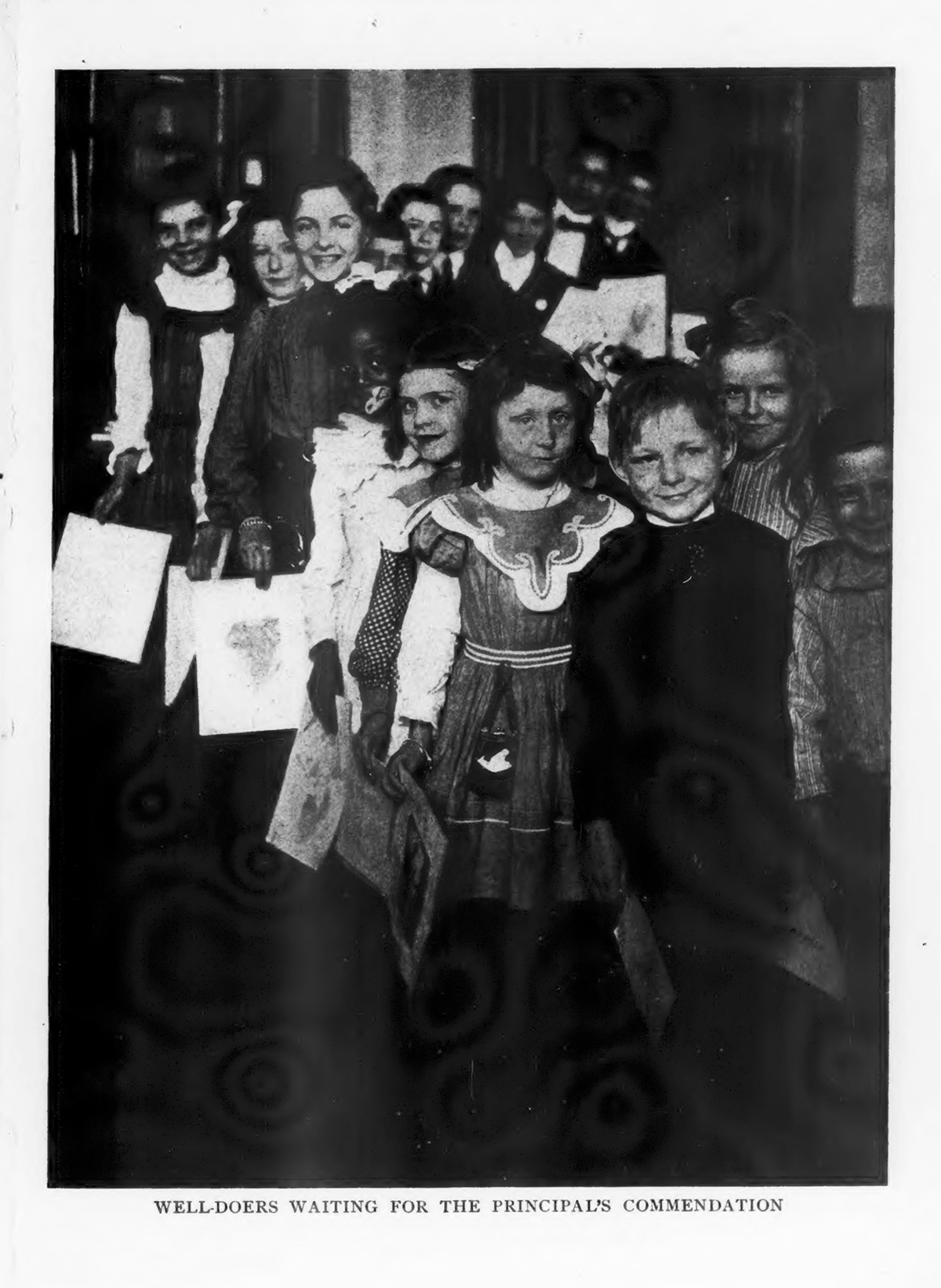 Schoolchildren of different ages are lined up, holding documents in their hands. Original caption reads "Well-Doers Waiting for the Principal's Commendation"