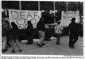 Protestors outside of a school holding signs. One says, "Deaf CEO Now!"